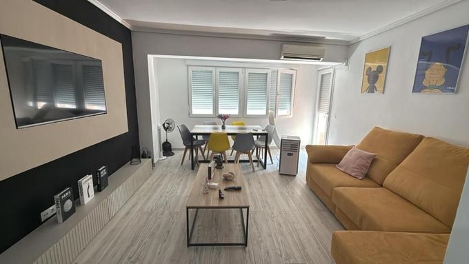 Sala de estar moderna con sofá color beige, mesa de centro, zona de comedor, cuadros en la pared y grandes ventanales.