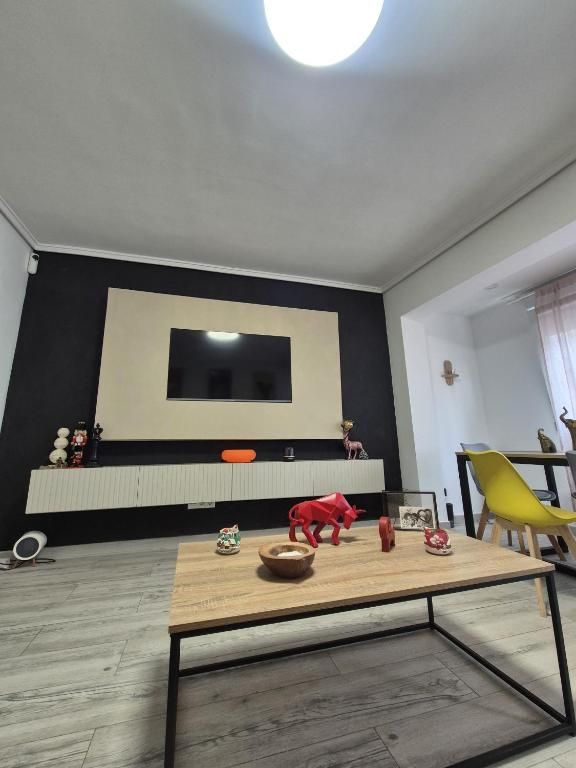 Sala de estar moderna con pared decorativa negra, televisor, radiador blanco y mesa de centro en primer plano.