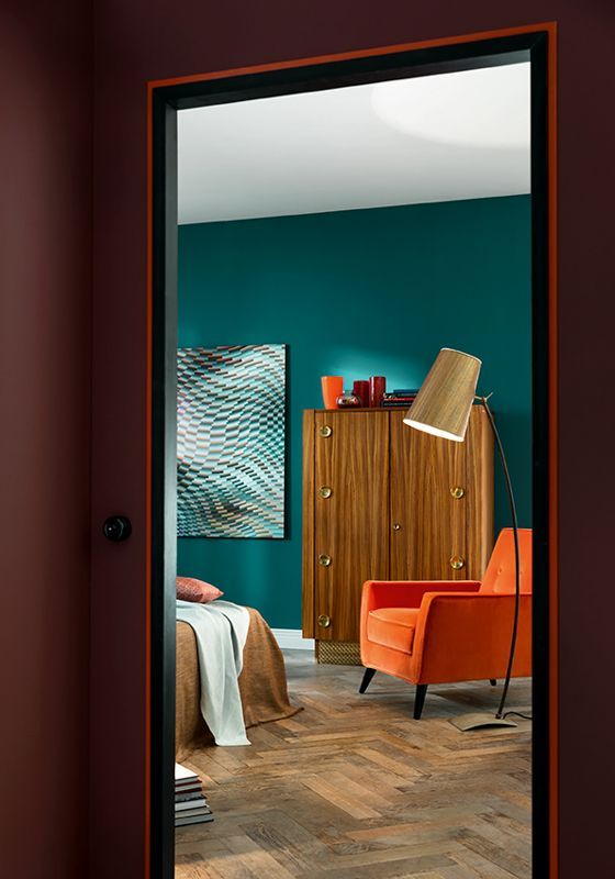 Ein Schlafzimmer mit blaugrünen Wänden und einem orangefarbenen Stuhl