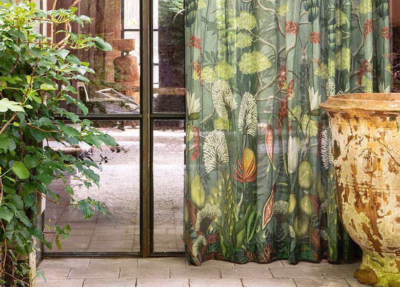 An einem Fenster hängt ein grüner Vorhang mit Blumenmuster.