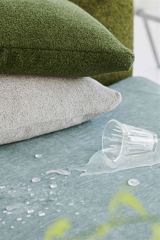 Auf einem Tisch liegt ein Stapel Kissen, aus dem ein Glas Wasser herausquillt.