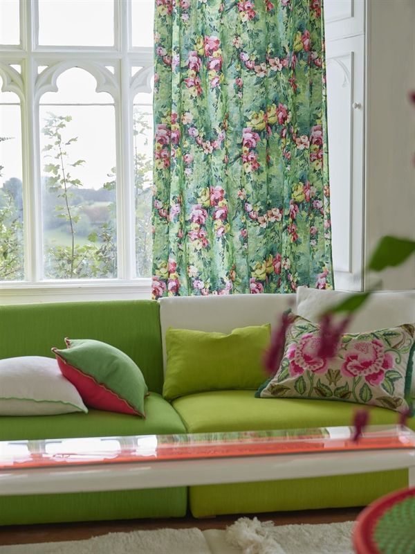 Ein Wohnzimmer mit einer grünen Couch und geblümten Vorhängen