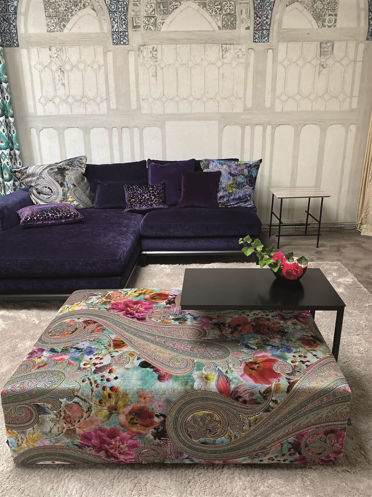 Ein Wohnzimmer mit einem lilafarbenen Sofa und einem geblümten Ottoman