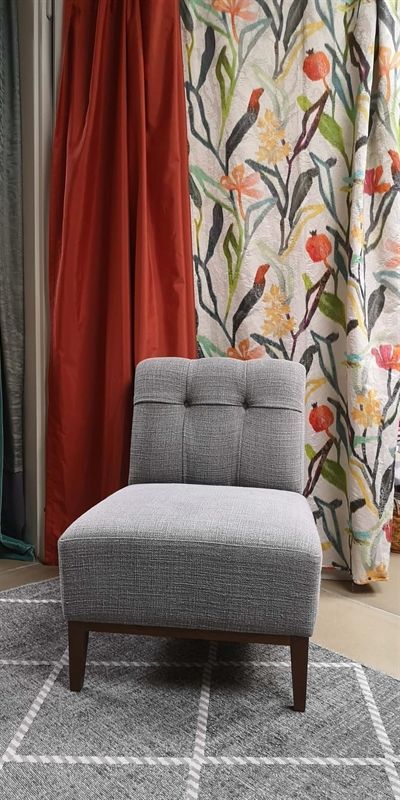 Ein grauer Stuhl steht auf einem Teppich vor einem geblümten Vorhang.