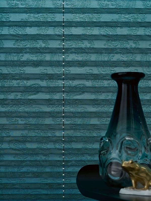 Eine Vase mit einem Gesicht darauf steht auf einem Tisch vor einer blauen Jalousie.