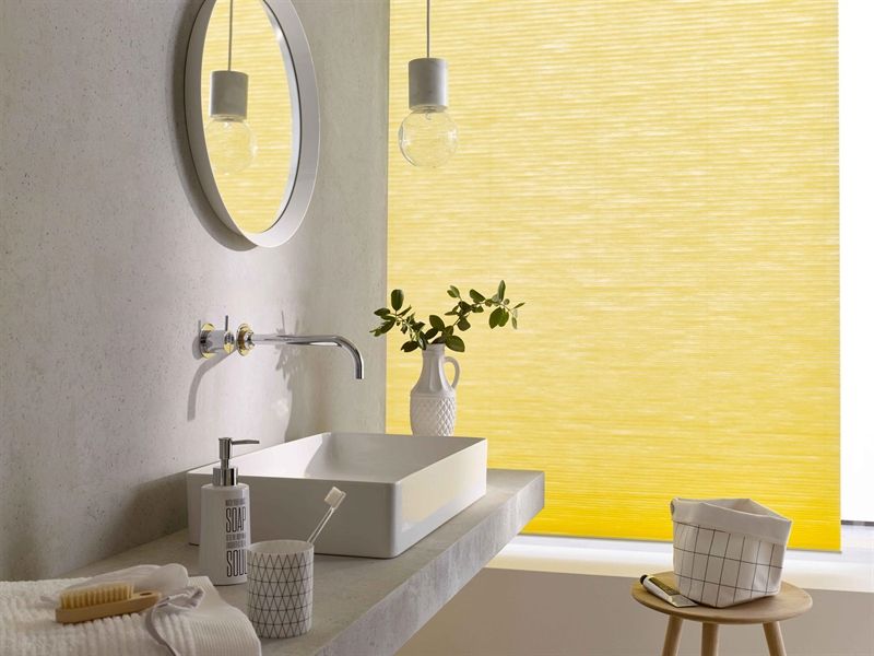 Ein Badezimmer mit Waschbecken, Spiegel und gelben Jalousien