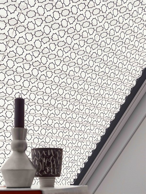 Auf einem Tisch vor einem Fenster steht eine Kerze mit einem Muster darauf.