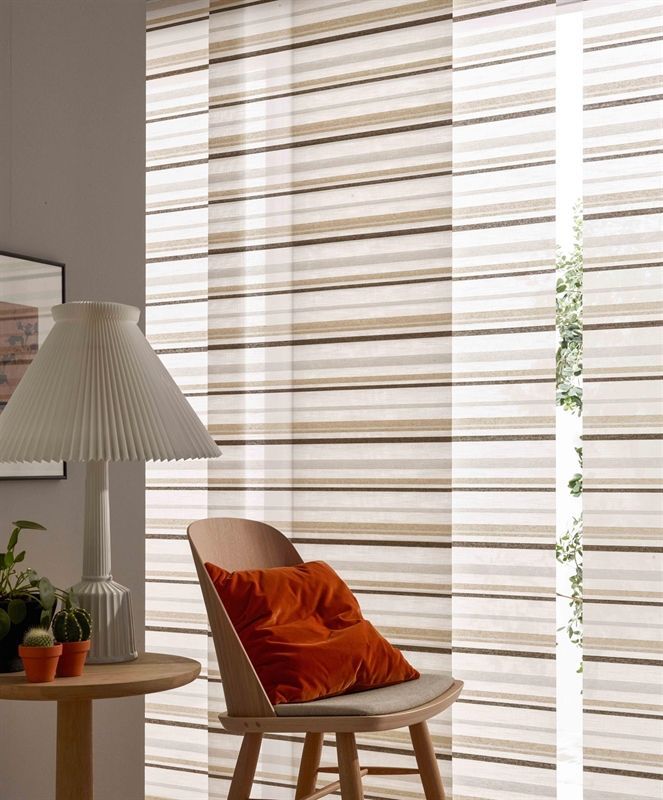 Ein Stuhl mit einem orangefarbenen Kissen steht vor einem Fenster mit gestreiften Vorhängen