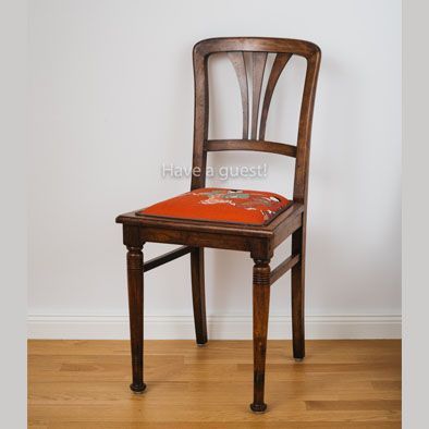 Ein Holzstuhl mit einem roten Sitzkissen mit der Aufschrift „Ich habe einen Gast“