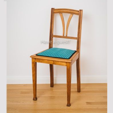 Ein Holzstuhl mit blauem Sitzkissen sagt: „Ich habe einen Gast“