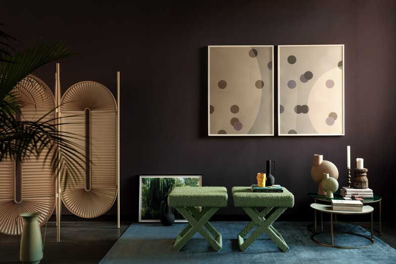 Ein Wohnzimmer mit zwei grünen Ottomanen und zwei Gemälden an der Wand