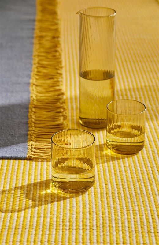 Ein Krug und zwei Gläser Wasser stehen auf einem gelb gestreiften Teppich.