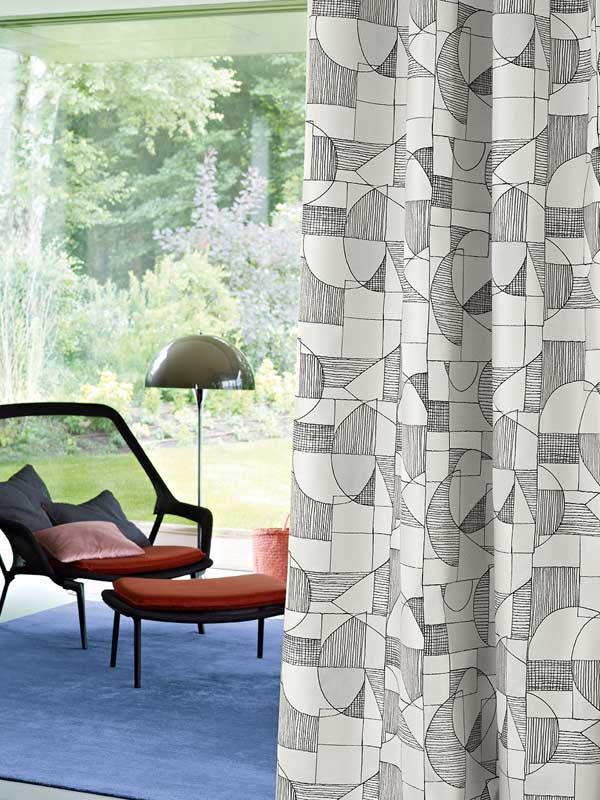 Ein Wohnzimmer mit Sessel und Ottomane vor einem großen Fenster