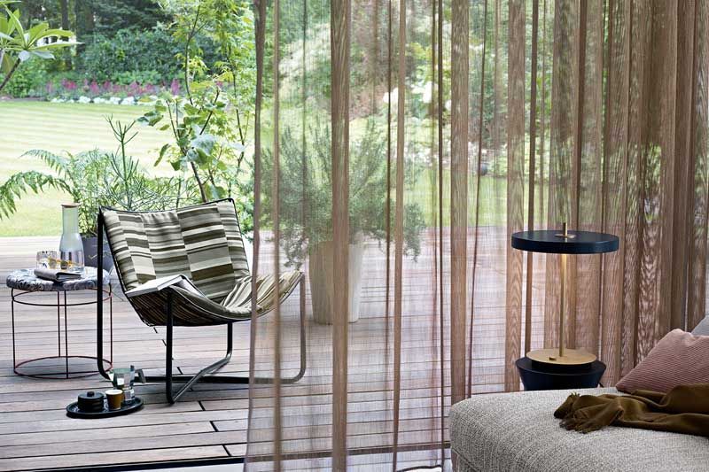 Ein Wohnzimmer mit Couch, Sessel, Tisch und Vorhängen.