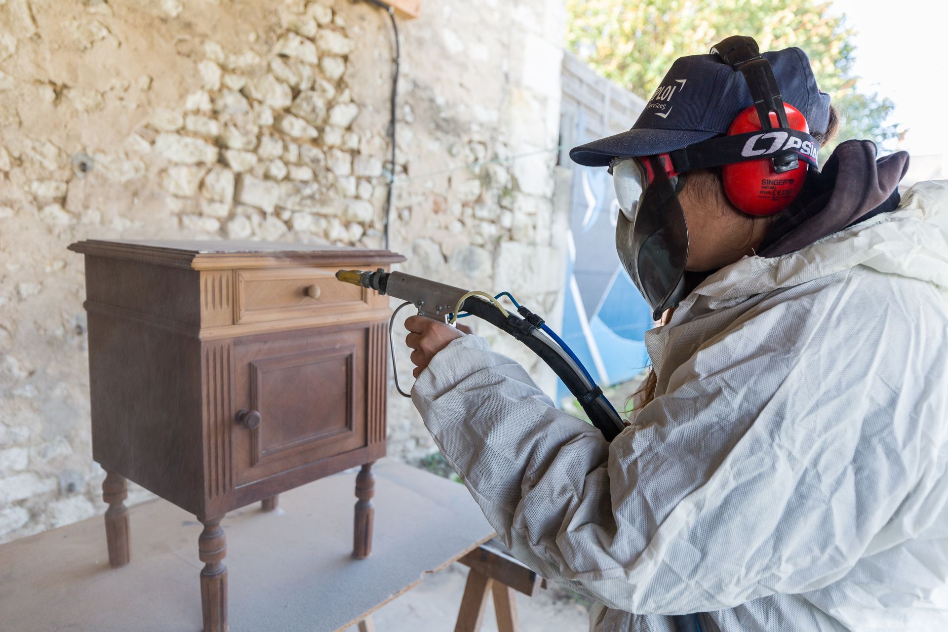 Professionnelle d'EMPLOI PLURI-SERVICES en combinaison blanche s'occupant de poncer une table de nuit