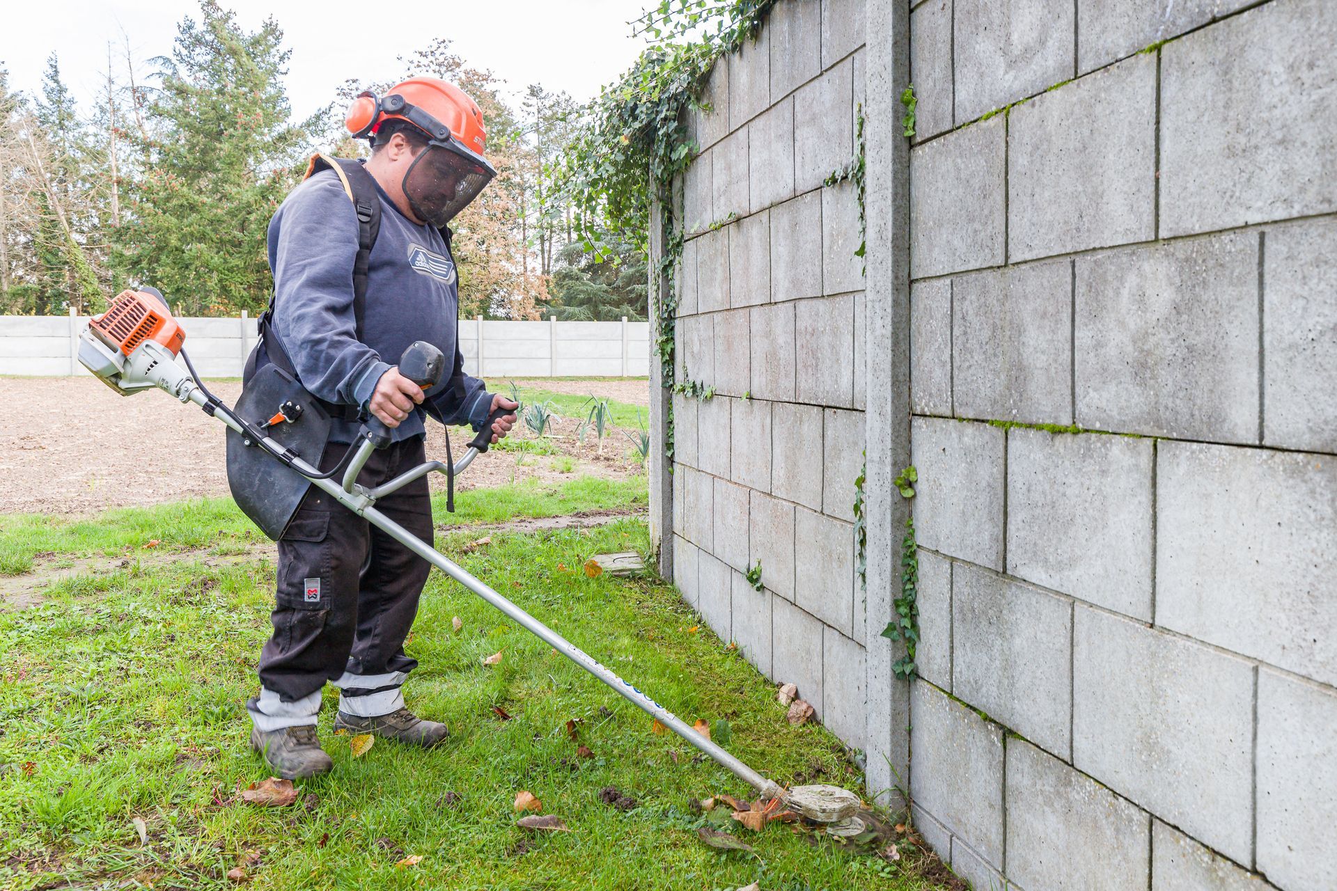 Professionnel d'EMPLOI PLURI-SERVICES coupant des mauvaises herbes près d'un mur