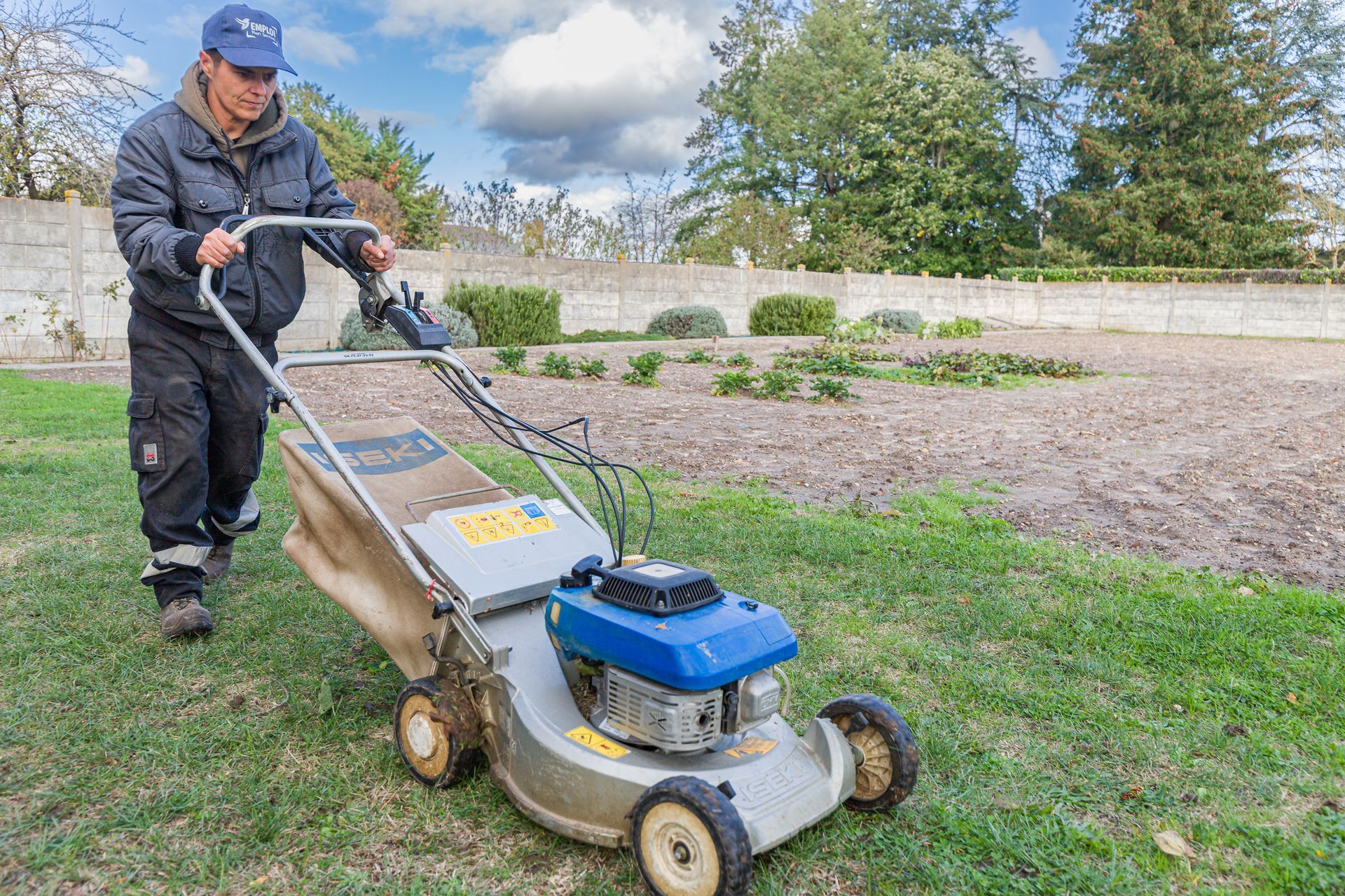 Professionnel d'EMPLOI PLURI SERVICES passant la tondeuse dans un jardin