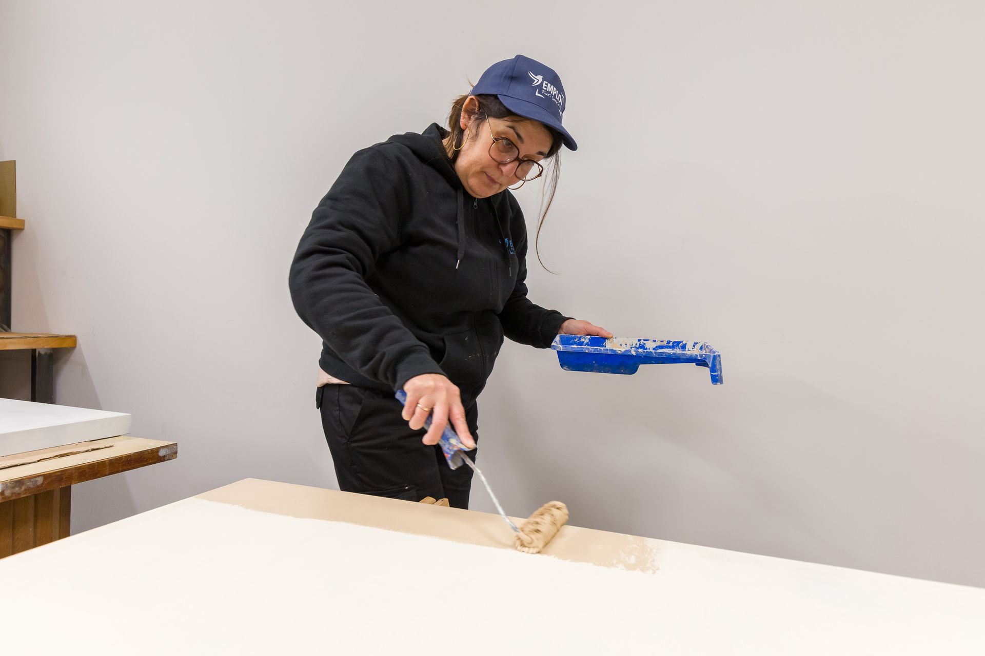 Professionnelle d'EMPLOI PLURI-SERVICES passant un rouleau de peinture sur une planche de bois.