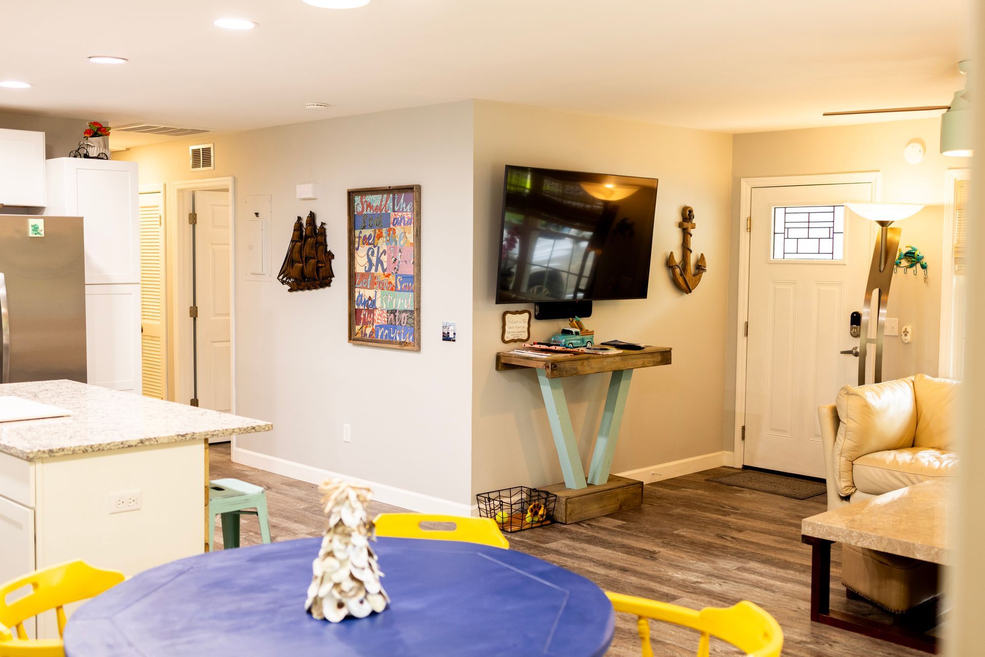 A living room with a blue table , yellow chairs , and a flat screen tv.