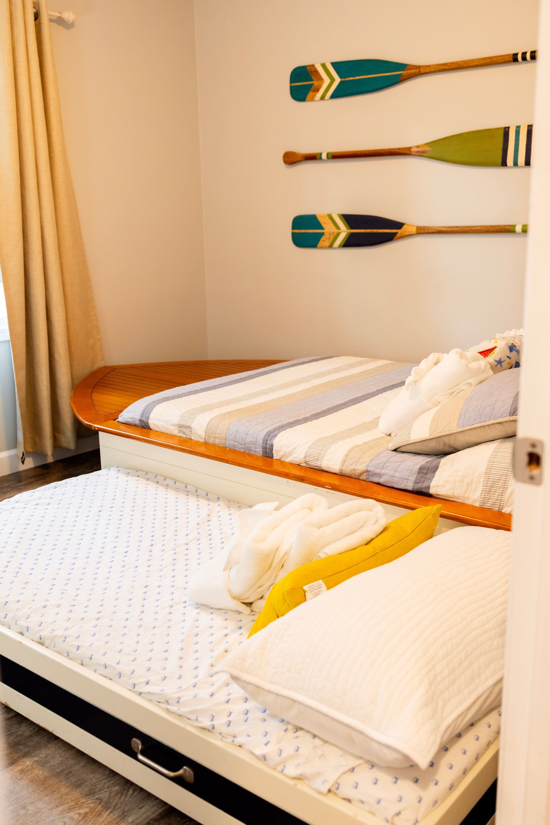 A bedroom with two beds and three oars on the wall.