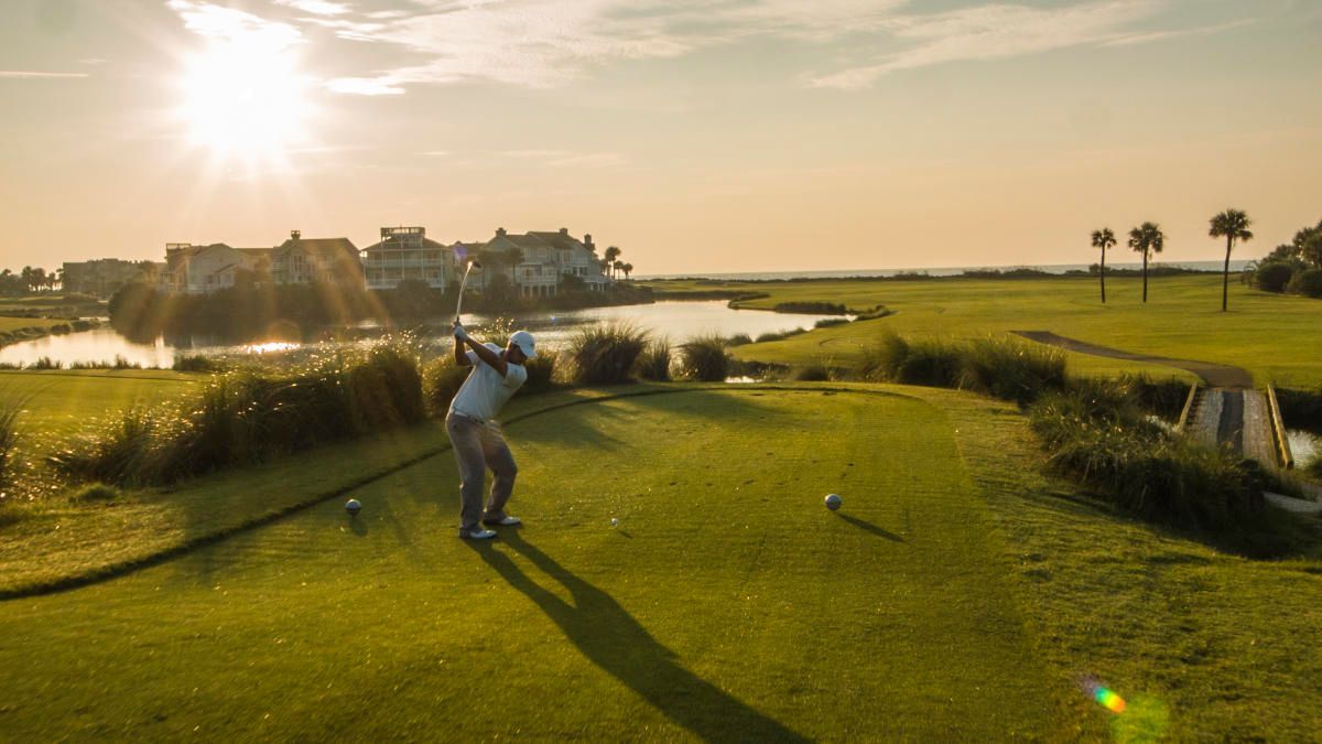 A man is swinging a golf club on a golf course at sunset.
