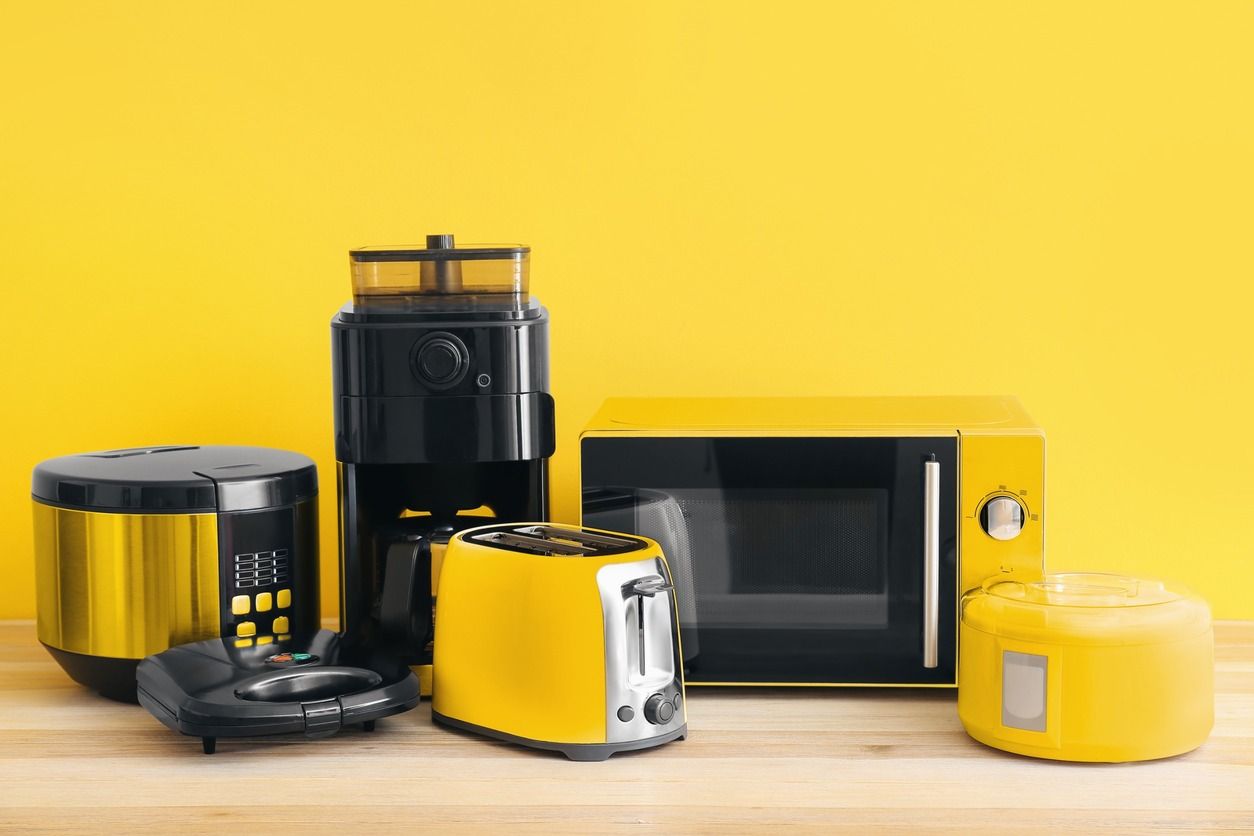 Un microondas, una cafetera, una tostadora y una olla arrocera están sobre una mesa de madera.