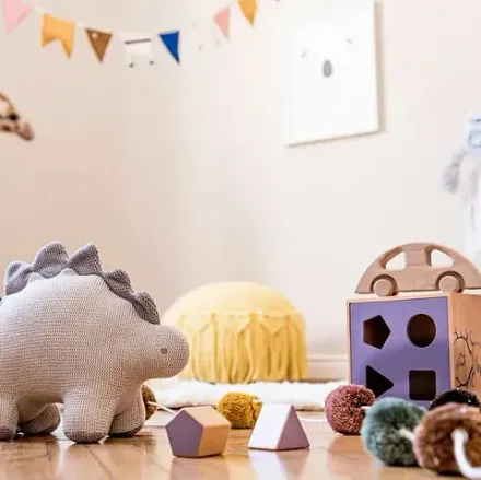 Un dinosaurio de peluche está sentado en el suelo rodeado de juguetes.