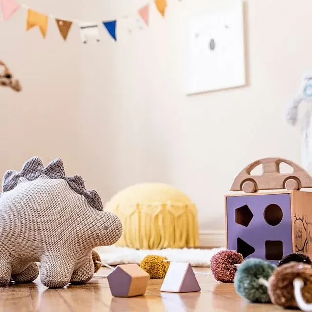 Un dinosaurio de peluche está sentado en un piso de madera rodeado de juguetes.