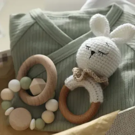 Un sonajero de conejo tejido a crochet y un mordedor de madera se encuentran encima de una camisa verde.