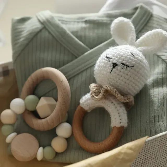 Un conejito de ganchillo está sentado junto a un mordedor de madera.