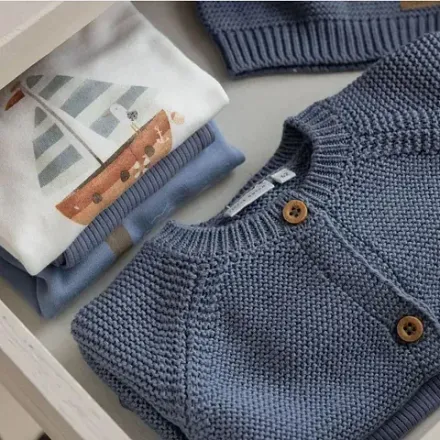 Un cajón lleno de ropa de bebé, incluido un suéter azul.