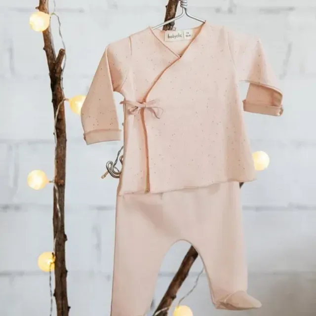 Un conjunto de ropa de bebé está colgado en la rama de un árbol.