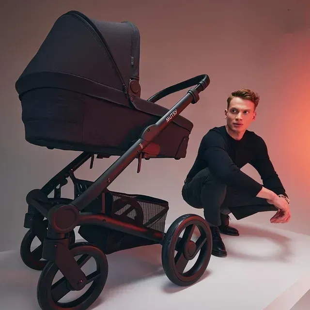 Un hombre en cuclillas junto a un cochecito que dice