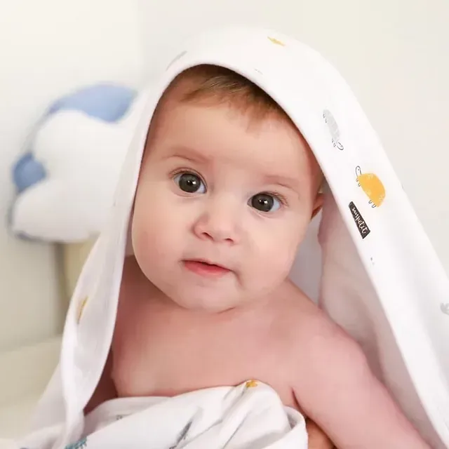 Un bebé está envuelto en una toalla blanca y mira a la cámara.