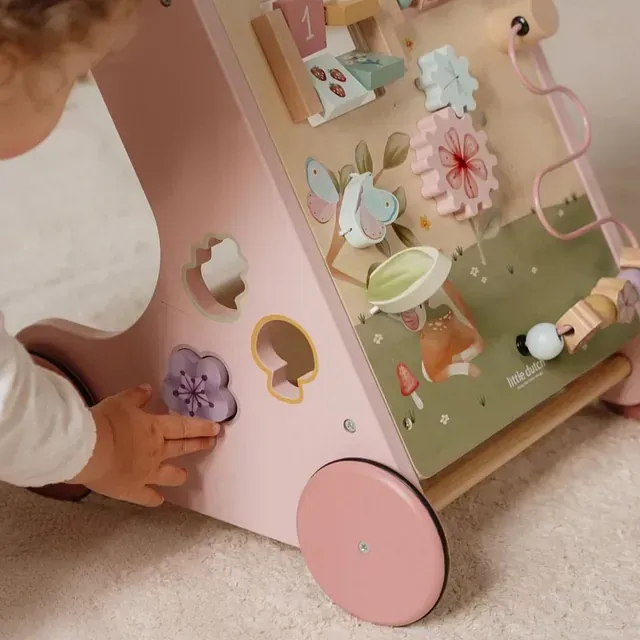 Un bebé está jugando con un andador de madera rosa.