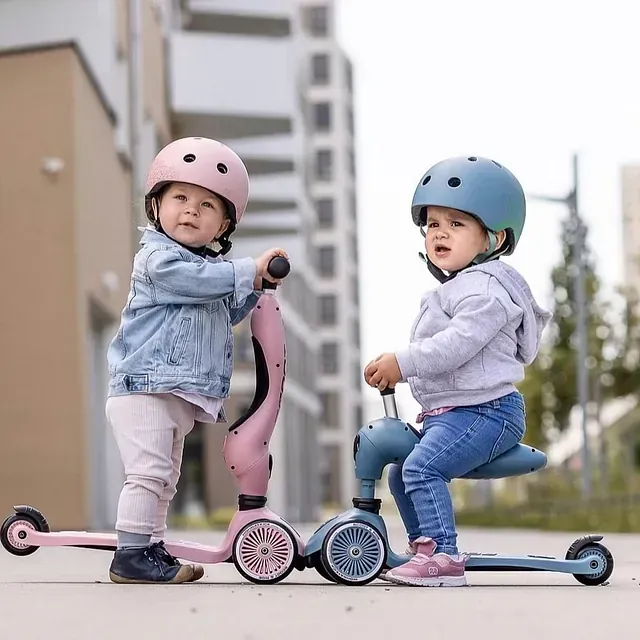 Dos niños pequeños andan en patinete por la calle.