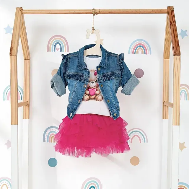 Una chaqueta vaquera de niña y un tutú rosa están colgados en un perchero.
