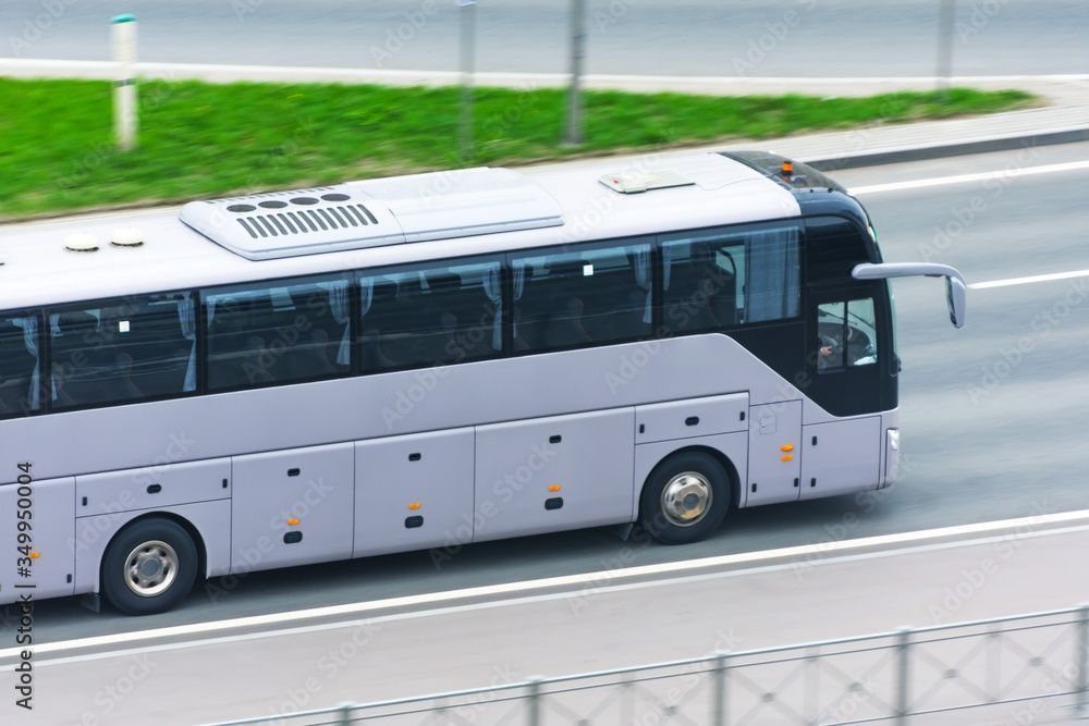 Grauer Reisebus fährt auf einer mehrspurigen Strasse, im Hintergrund grünes Gras.