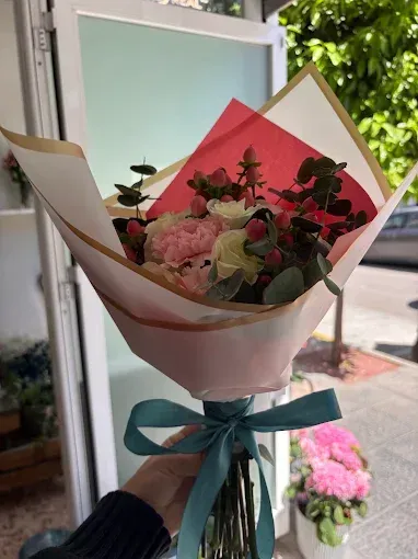 Ramo de flores rosas envuelto en papel blanco y rosa con una cinta verde azulado junto a una puerta