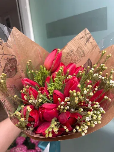 Ramo de tulipanes rojos con paniculata, envuelto en papel marrón y sostenido con una mano