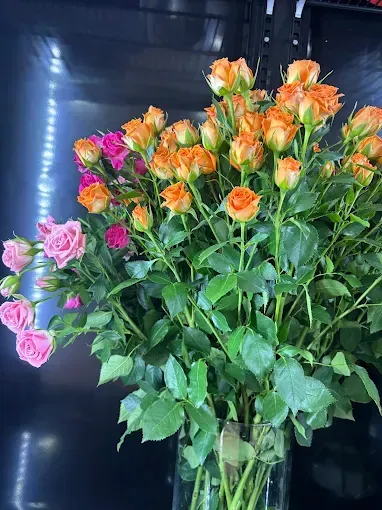 Ramo de rosas naranjas y rosas en un jarrón transparente sobre un fondo oscuro