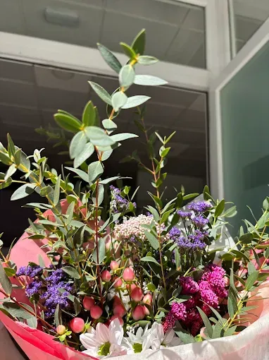 Colorido ramo de flores silvestres en tonos rosas, morados, blancos y verdes, con un edificio moderno de fondo