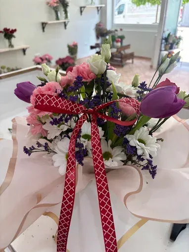 Arreglo de flores rosas y moradas atado con una cinta roja sobre una mesa en una habitación luminosa