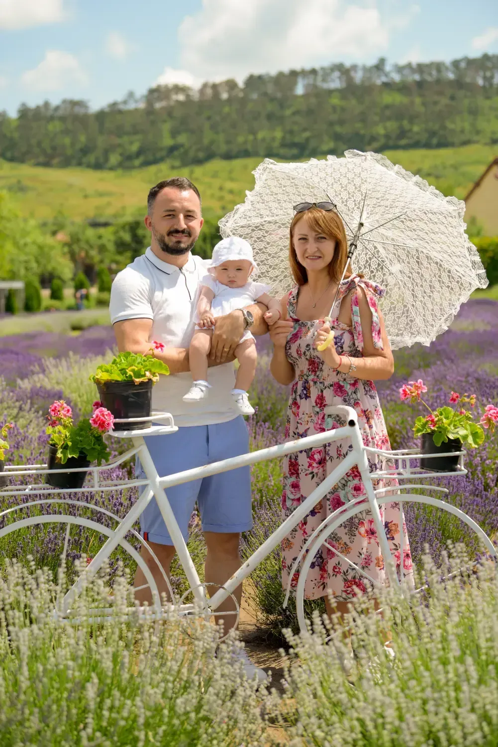 Familia de pie junto a una bicicleta blanca en un campo de flores; una mujer sostiene una sombrilla.