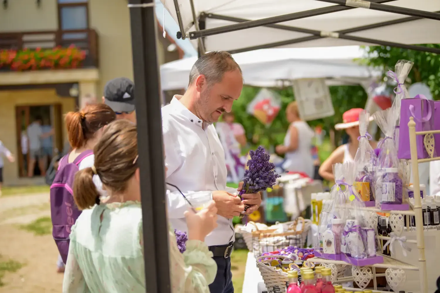 Gente mirando lavanda y productos artesanales en un puesto de mercado al aire libre.