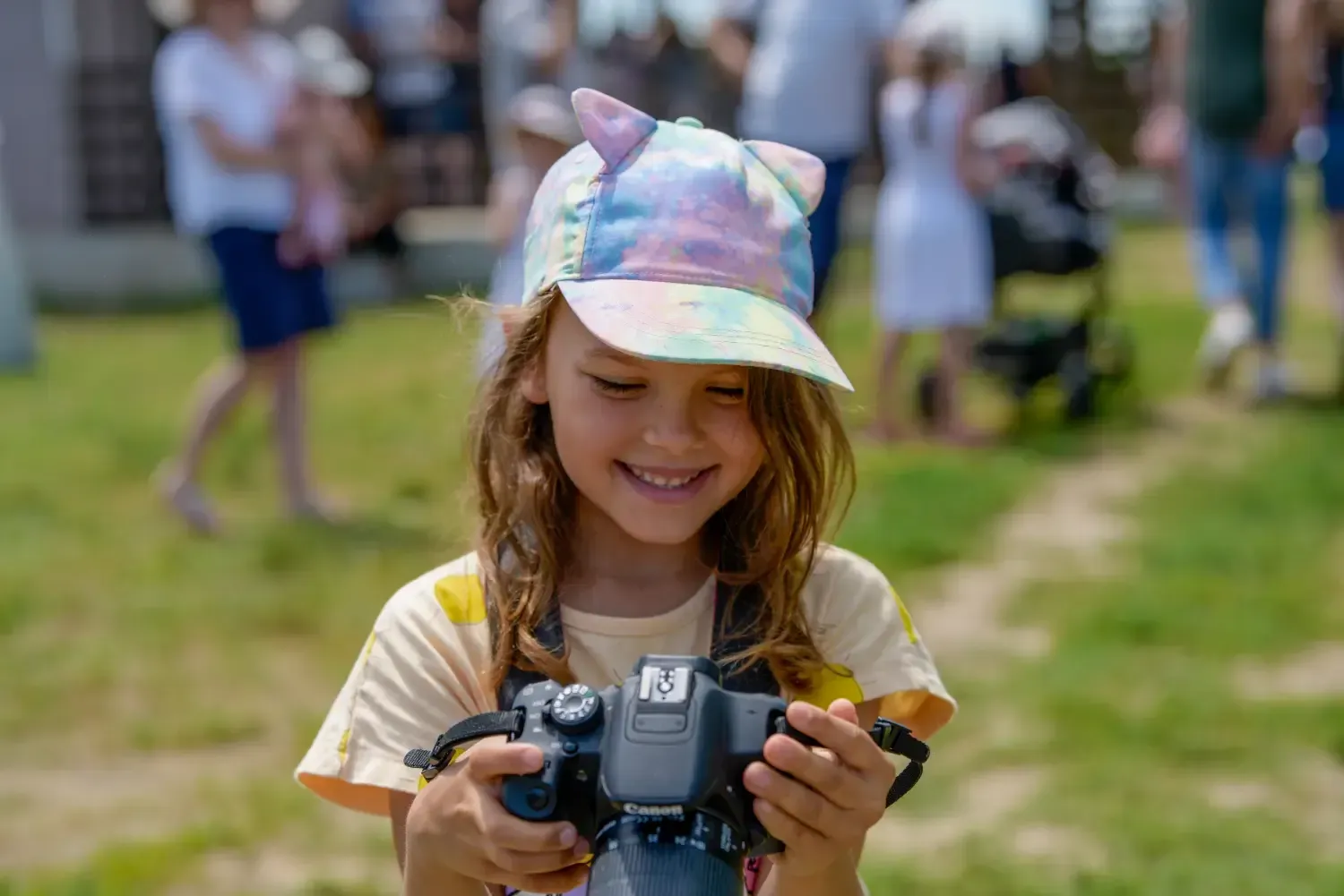 Un niño sonriente con una gorra de color pastel mira a una cámara al aire libre en un campo de hierba.