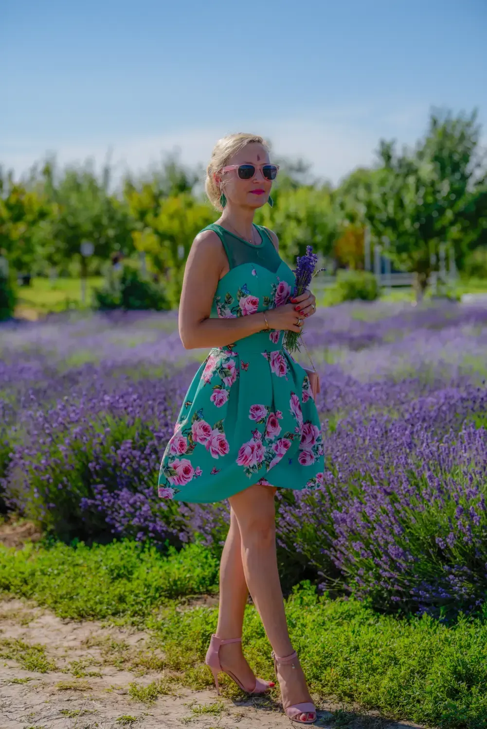 Mujer con un vestido verde estampado de flores de pie en un campo de lavanda en un día soleado.