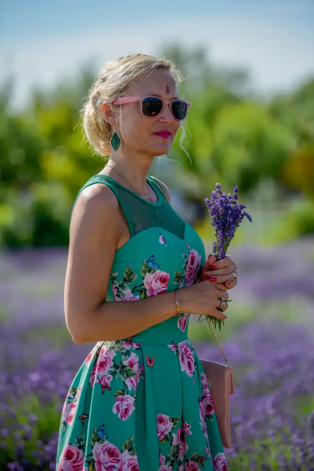 Mujer con vestido verde estampado de flores sosteniendo flores moradas en un campo de lavanda.