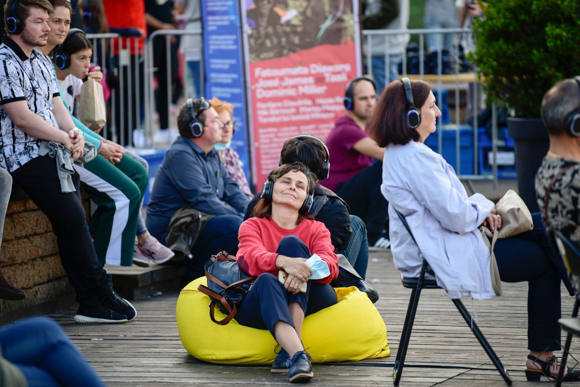Personas sentadas en bancos y pufs en un evento al aire libre, con auriculares puestos y mirando algo que estaba por venir.