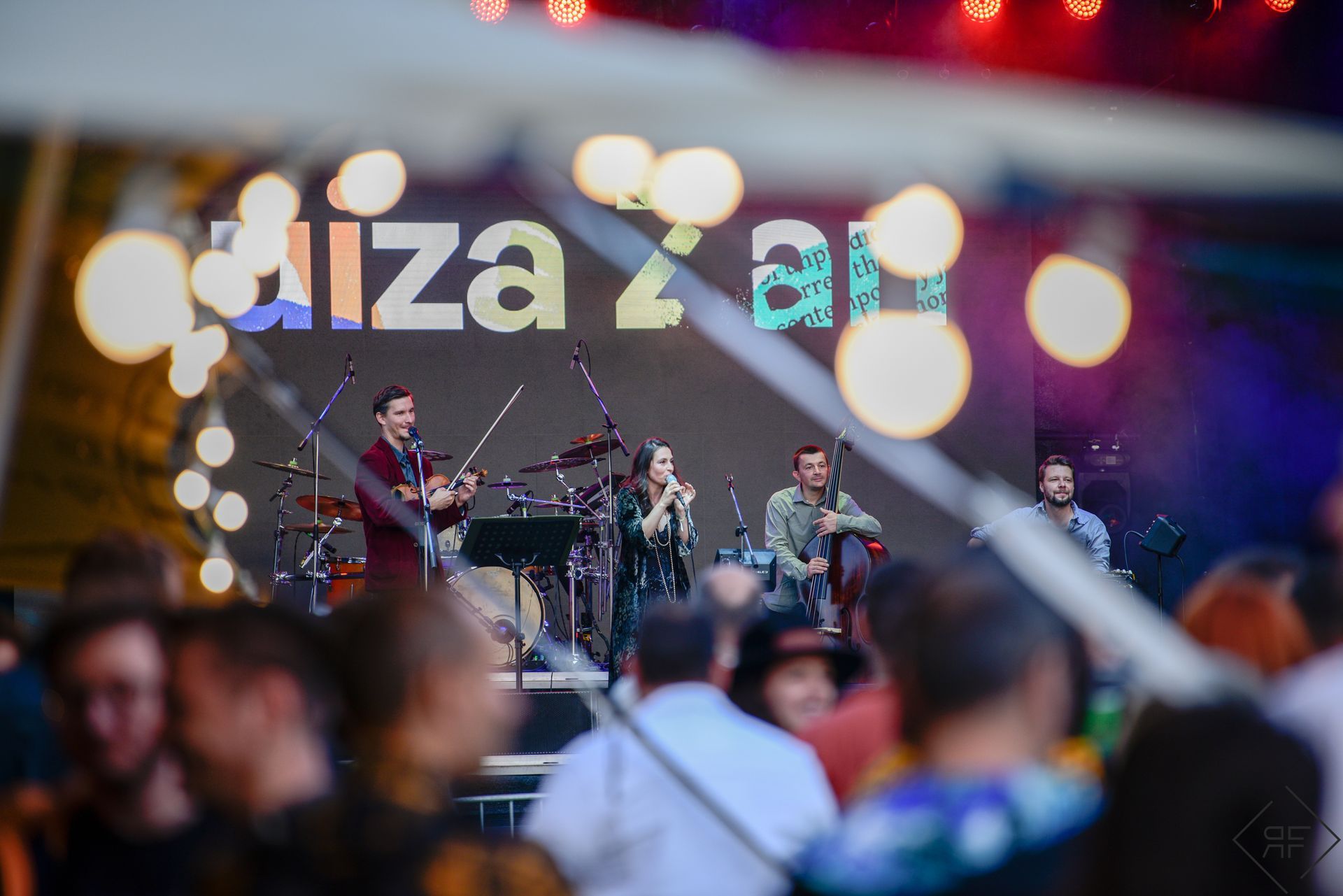 Actuación de una banda en vivo al aire libre en un escenario iluminado con el público borroso en primer plano.